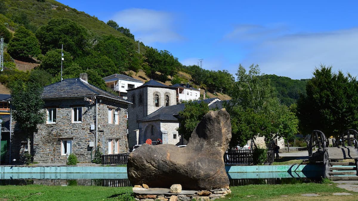 Escultura de piedra en Balboa con vistas a la iglesia y casas de pizarra del pueblo.