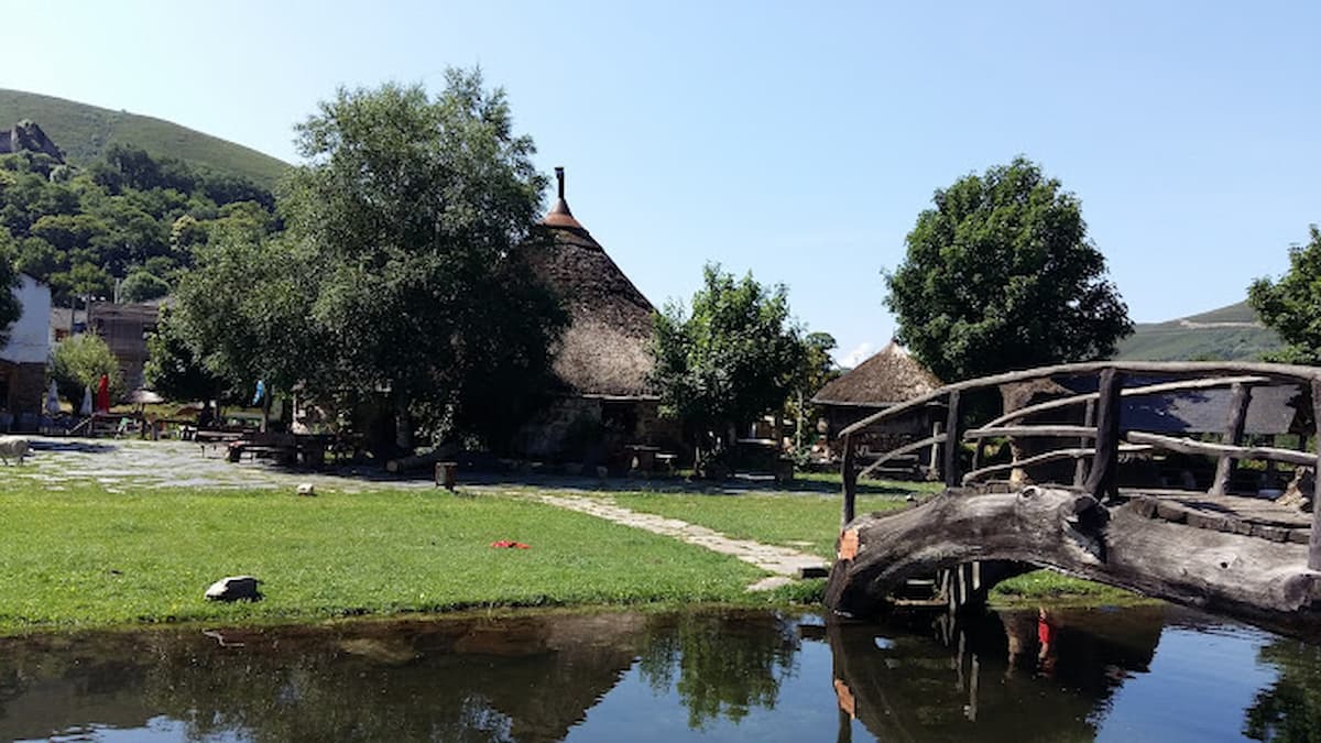 Puente de madera sobre el río con pallozas y praderas verdes en Balboa, León.