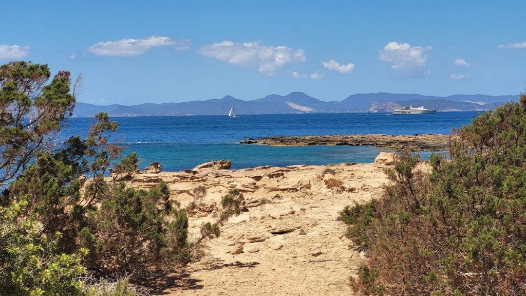 Vista de la costa rocosa con el mar azul y un velero en el horizonte en Mallorca.