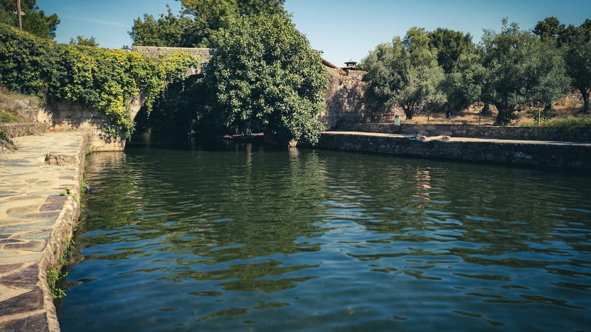 Piscina natural de Acebo con un puente de piedra cubierto de vegetación.
