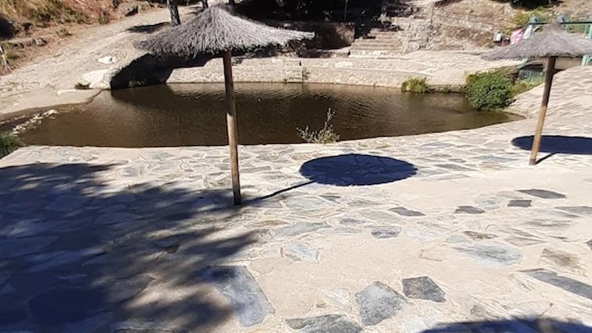Piscina natural de Acebo con sombrillas de paja y rodeada de árboles.