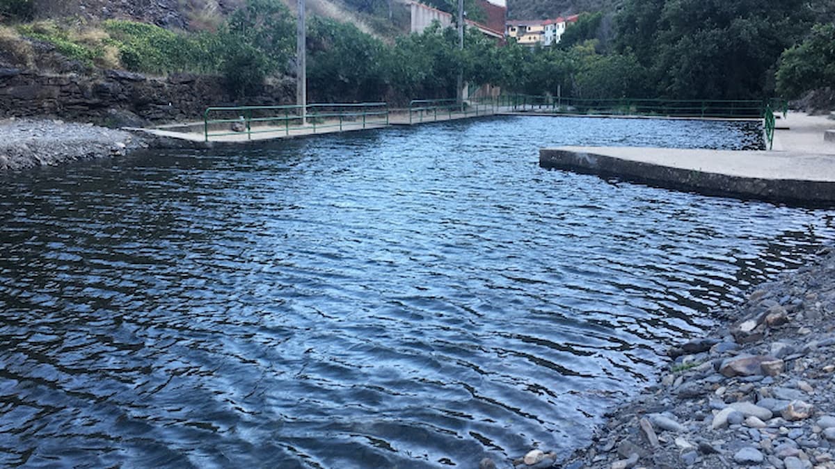 Reflejo del agua en la piscina natural de Valero con piedras en la orilla y barandillas de seguridad.