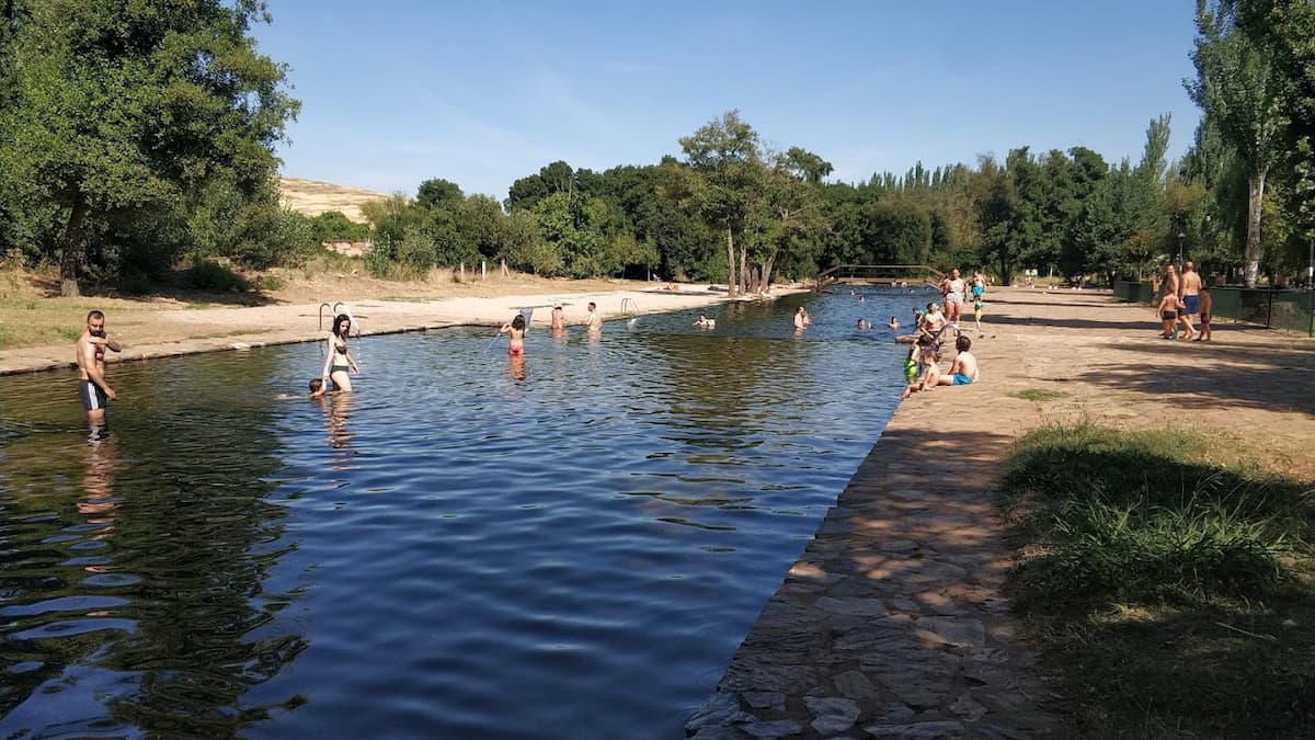 Bañistas disfrutando de la piscina natural de La Codosera, rodeada de árboles y con amplias zonas de descanso.