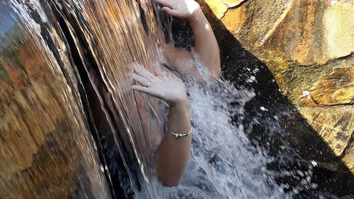 Pequeña cascada en la piscina natural de La Codosera, con una persona bajo el agua disfrutando del hidromasaje natural.
