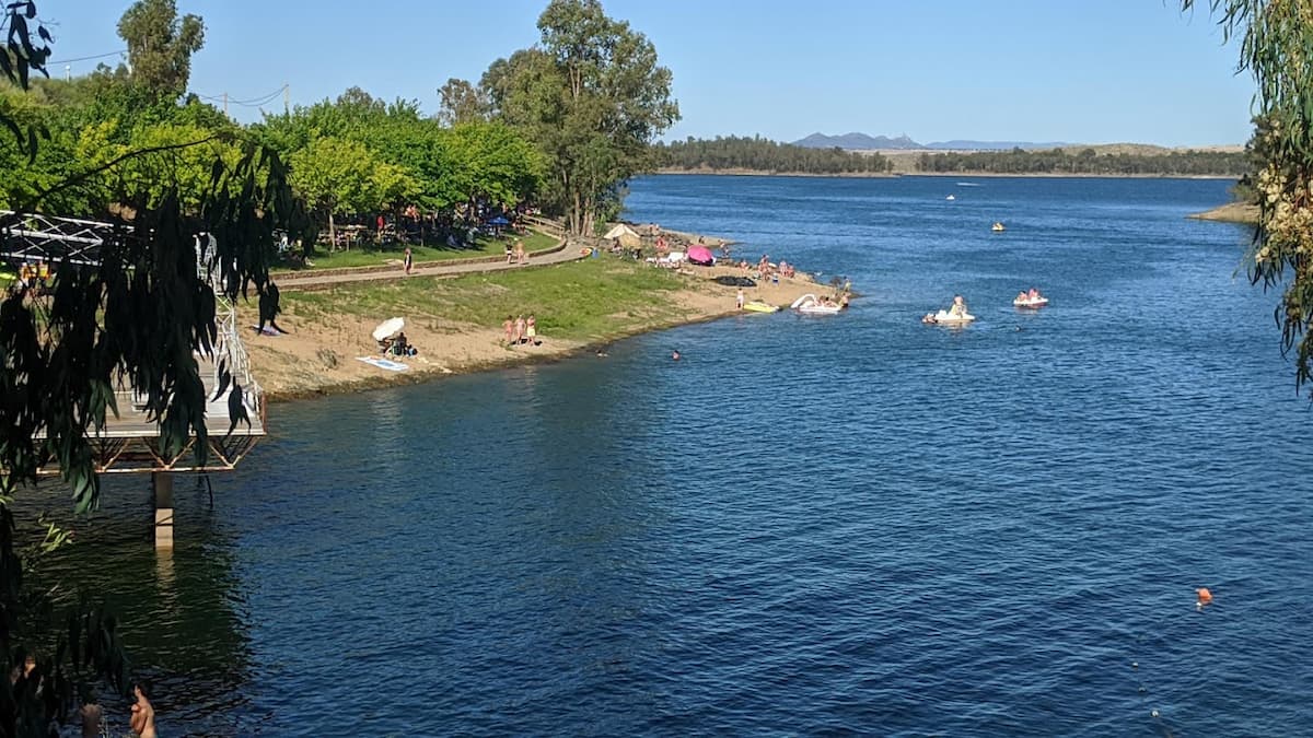 Vista panorámica del embalse de Orellana con bañistas y embarcaciones recreativas en el agua.